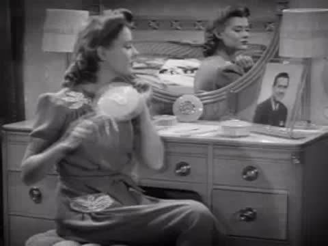 Woman sitting at a dressing table brushing her hair, 1940s bedroom