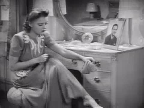 Woman seated at a vanity putting on stockings, 1940s bedroom