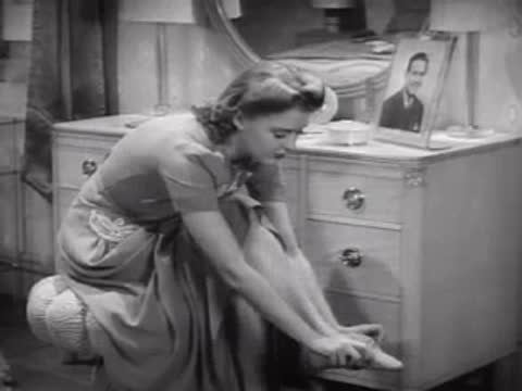 Woman leaning forward to put on stockings at a vanity, bedroom