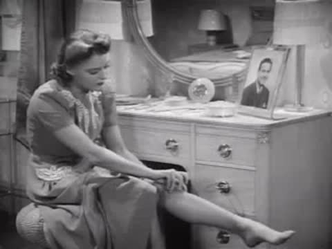 Woman adjusting stockings while seated at a vanity, 1940s bedroom