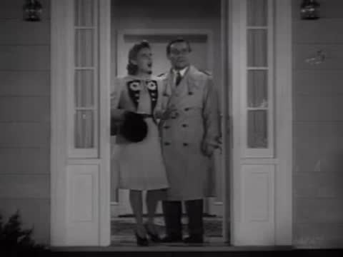 Woman entering a house where a man waits at the open door