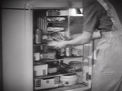 Person opening a refrigerator and loading food trays, 1940s kitchen