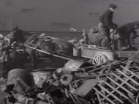Men loading scrap metal into a horse-drawn cart near industrial machinery.