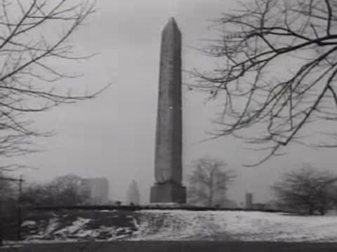 An Egyptian obelisk standing in a snowy park with bare trees.