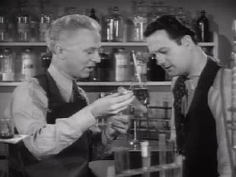 Two researchers pouring liquids between glass tubes in a laboratory.