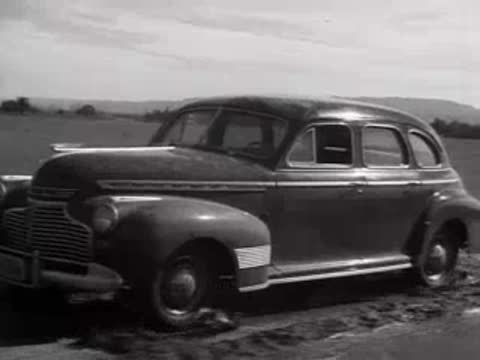 A 1940s sedan parked on an outdoor lot with trees in the background.