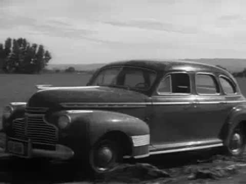 A modern 1940s sedan driving past another vehicle outdoors.