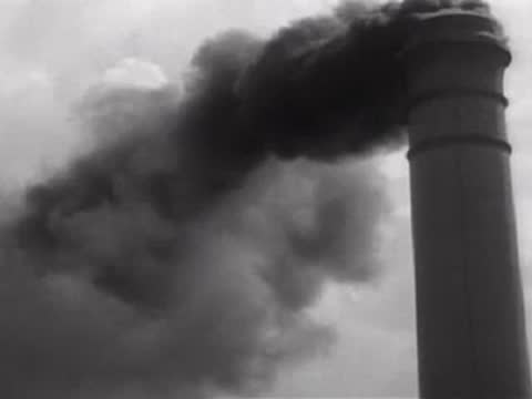 Thick black smoke pouring from an industrial smokestack against a cloudy sky.