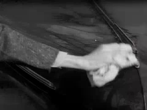 A person using a cloth to wipe down the hood of a car.