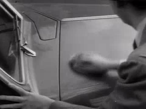 A worker polishing a car door panel by hand, mid-20th century.