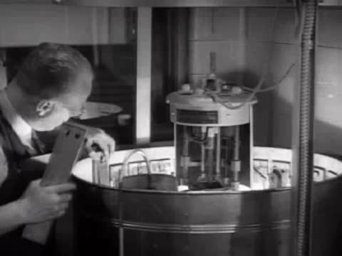 Close-up of a technician operating a cylindrical laboratory testing apparatus.