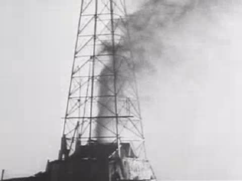 Industrial oil drilling derrick emitting dark smoke into the sky, 1940s.