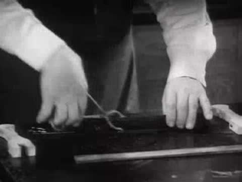 A pair of hands testing the flexibility of a black material strip using tongs.