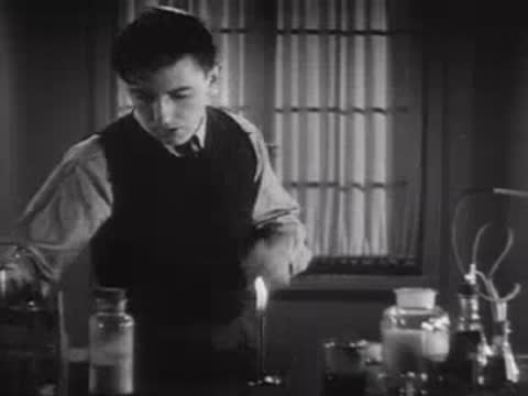 A young laboratory assistant working with scientific glassware and a burner.