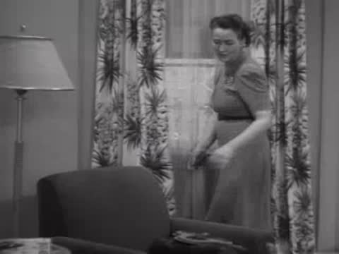 Woman walking across a living room toward a small appliance, 1940s interior