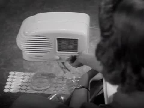Woman adjusting dials on a small white electric appliance, 1940s interior