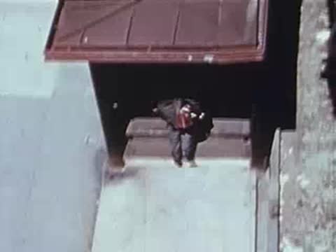 High-angle view of a man walking out of a building entrance on a sidewalk.