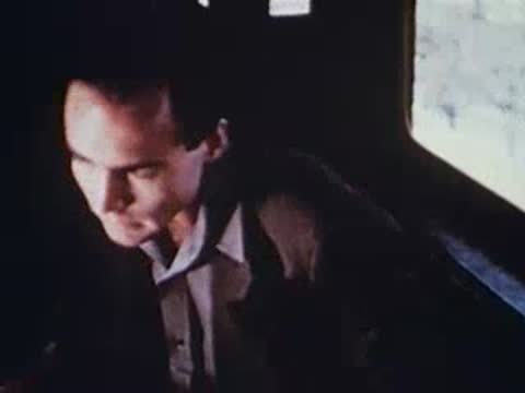 Man with dark hair sitting inside train, looking out window, archival footage.