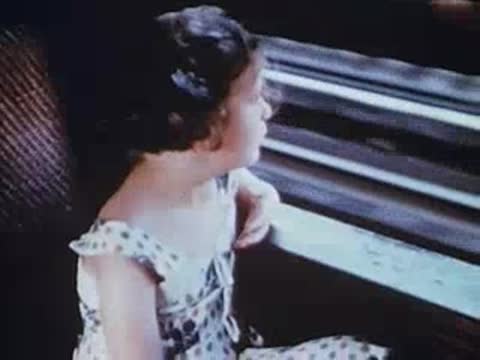 Young girl sitting inside moving train, looking out window, archival footage.