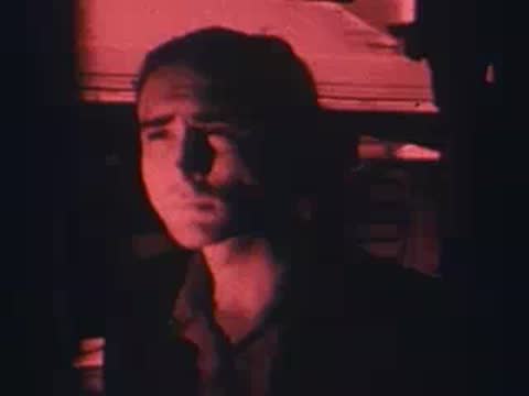 Man sitting inside dimly lit train interior, looking ahead, archival footage.
