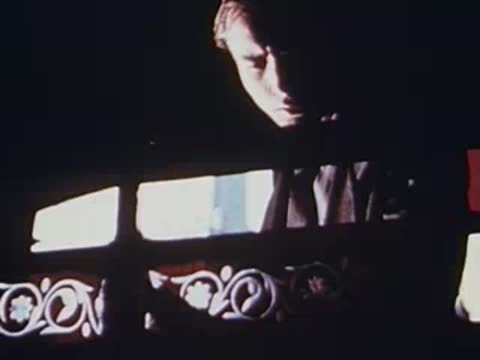 Man visible through train window with ornate decorative panels, archival footage.