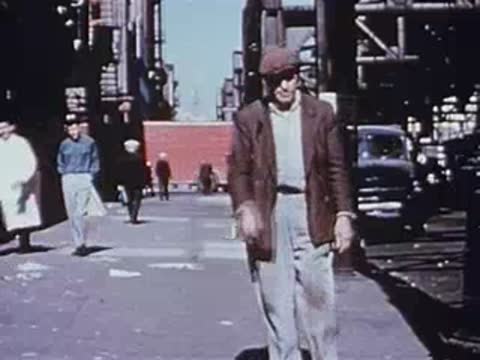 Man walking toward camera on city street, other pedestrians behind, archival footage.