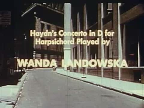 A curving paved street between tall buildings, with musician credits.