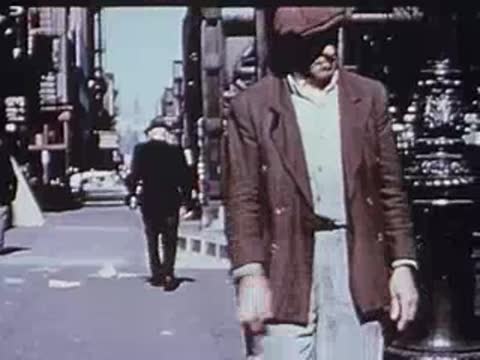 Older man walking down an urban sidewalk past elevated tracks.