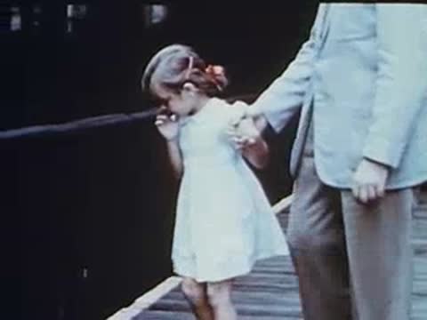 Little girl with man on elevated station platform pointing toward tracks.