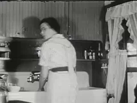 Woman standing in a vintage kitchen at the sink, washing dishes.