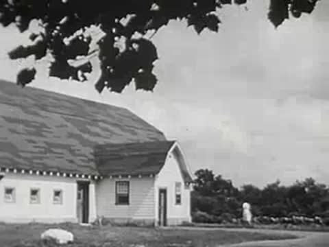 Exterior view of a farmhouse with a woman walking towards the entrance.