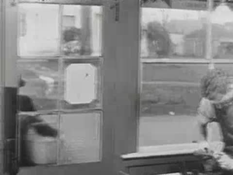 A person works behind a counter inside a shop, black and white.