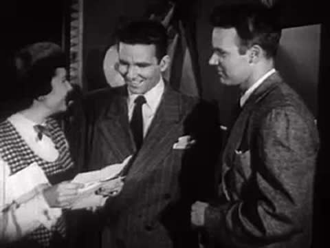 Four people standing together in an office reading papers and talking.