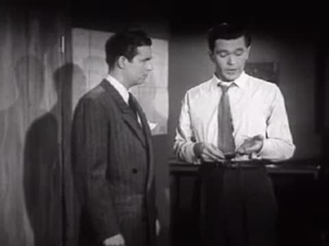 Man entering a room and greeting another man in a shirt and tie.
