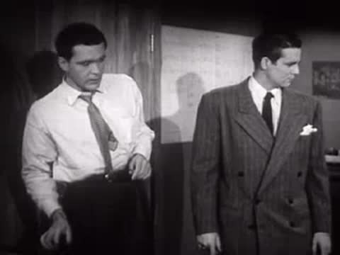 Two men talking in an office, one wearing a suit and one a shirt.