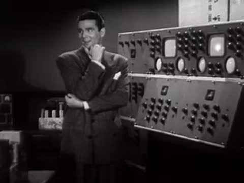 Man standing near a large electronic control panel with dials and switches.