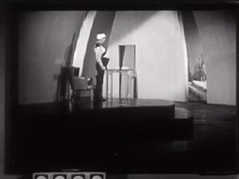 Two people in futuristic uniforms standing in a studio set with arched backdrop.