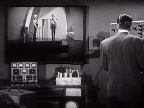 Man in suit observing a monitor showing two people in futuristic uniforms.