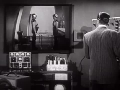Man in suit watching a monitor display of two people in uniform.