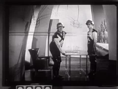 Two people in futuristic uniforms with superimposed diagrams on the screen.