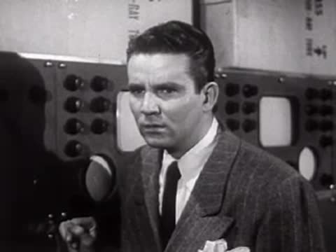 Man in suit talking in a laboratory with equipment behind him.