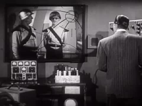 Man in suit watching a monitor screen showing two people in uniform.
