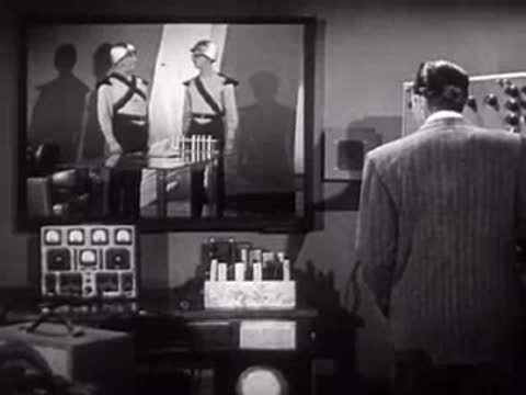 Man in suit observing a monitor screen showing two people in uniform.