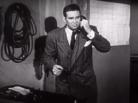 A man in a suit answers a telephone in an office, mid-century.