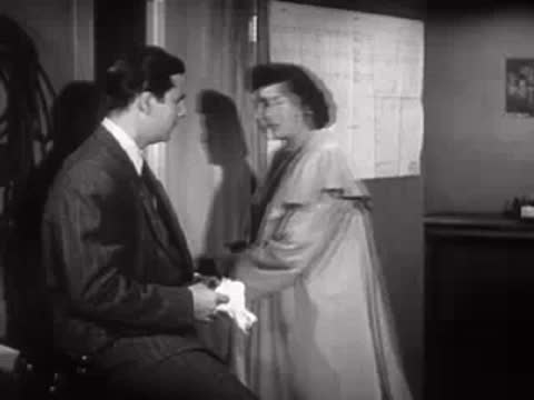 A man and woman talk in an office, mid-century workplace style.