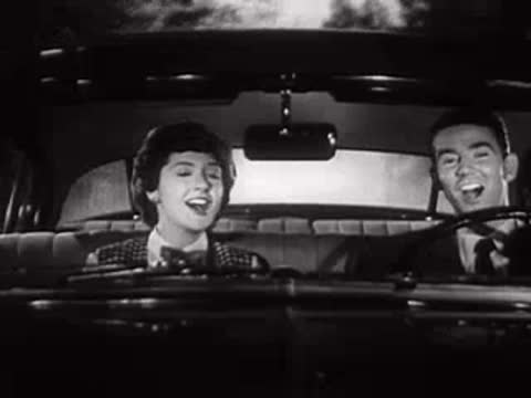 Two people smiling and talking inside a car in black and white.