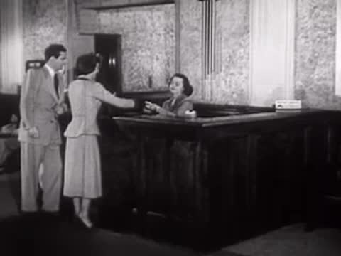 A man walks up to a desk in a public hall, mid-century style.