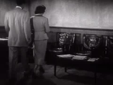 A man and woman walk into a waiting area and sit down, mid-century.