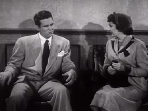 A man and woman sit together in a waiting room, mid-century style.