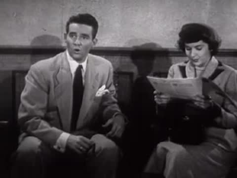 A man and woman react while sitting in a waiting room, mid-century style.
